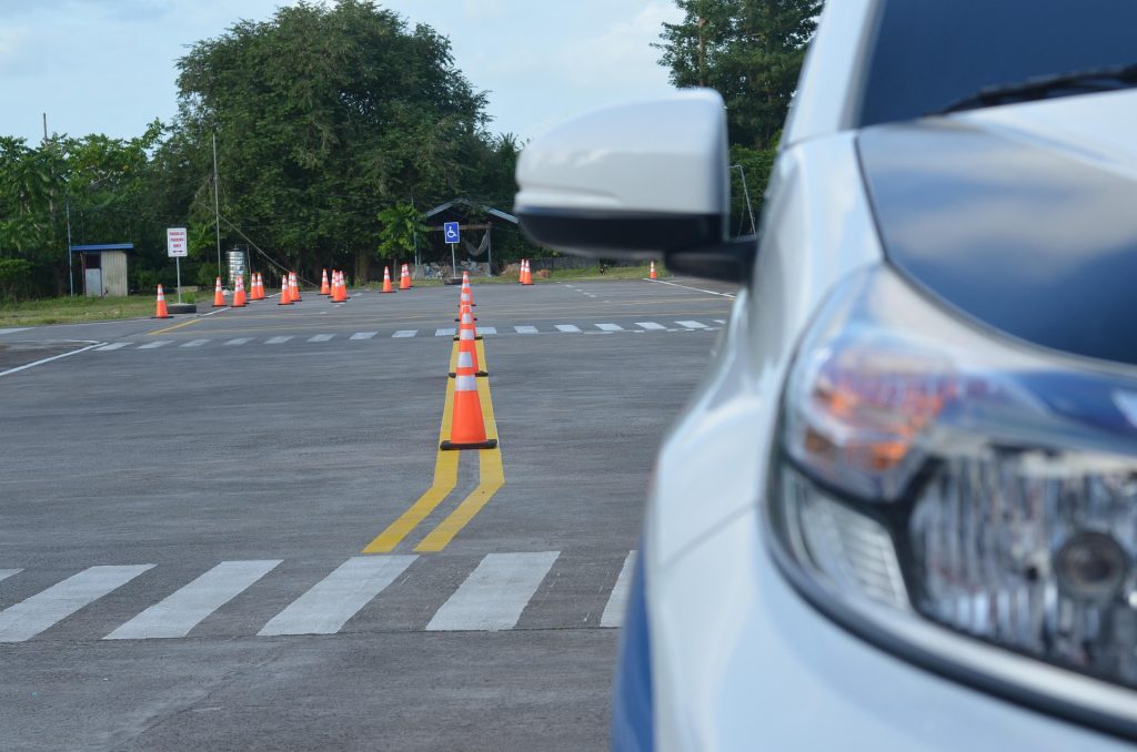 Car positioned beside traffic cones on a driving test practice course.